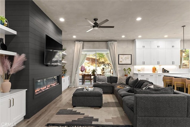 living room with ceiling fan, a large fireplace, light hardwood / wood-style floors, and wooden walls