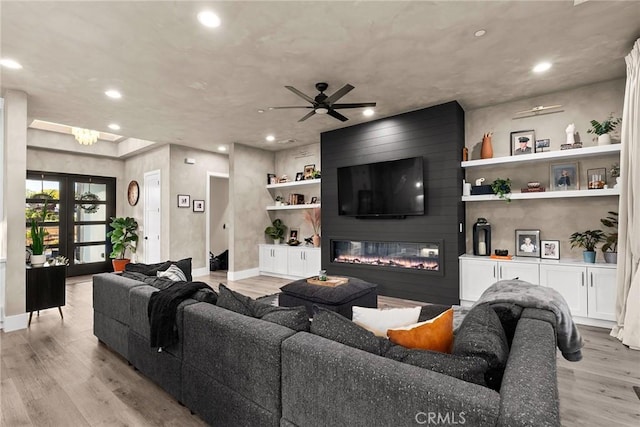 living room featuring ceiling fan, light wood-type flooring, a fireplace, and french doors