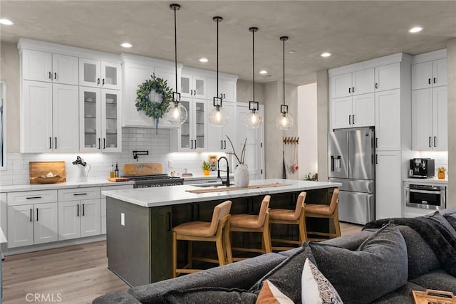 kitchen with appliances with stainless steel finishes, a breakfast bar, a kitchen island with sink, white cabinetry, and hanging light fixtures