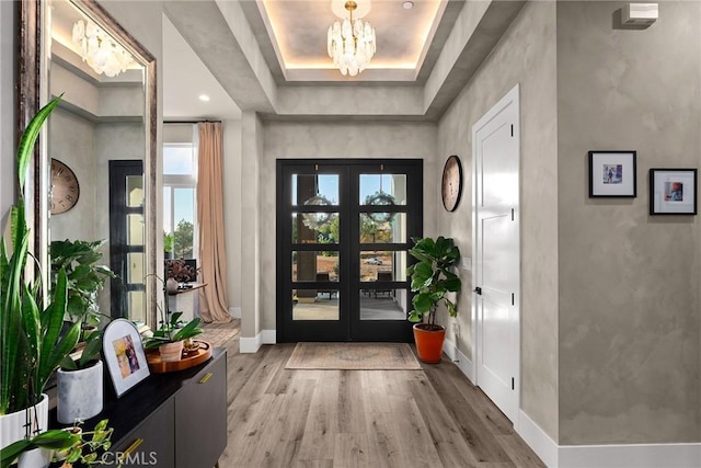 entryway with hardwood / wood-style flooring, an inviting chandelier, a tray ceiling, and french doors