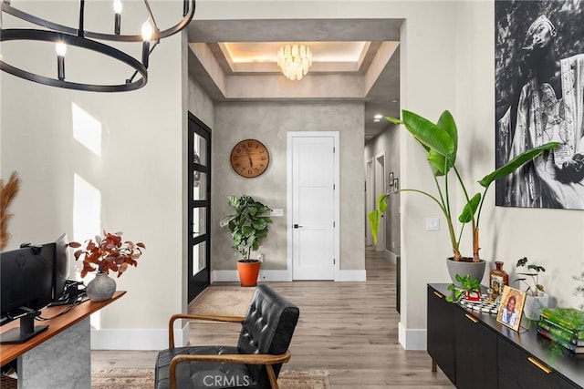 entrance foyer with light hardwood / wood-style floors, a raised ceiling, and an inviting chandelier