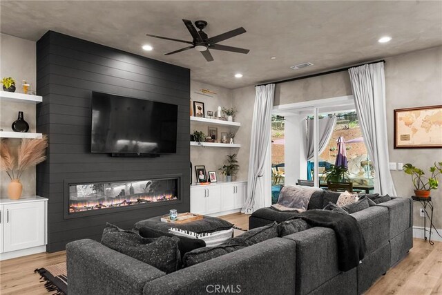 living room with a large fireplace, light hardwood / wood-style floors, and ceiling fan