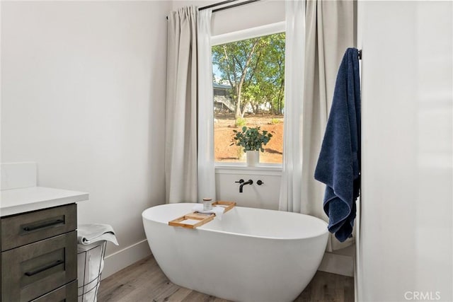 bathroom with a tub to relax in, a wealth of natural light, vanity, and hardwood / wood-style flooring