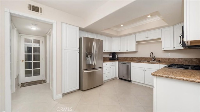 kitchen with appliances with stainless steel finishes, a tray ceiling, sink, white cabinets, and light tile patterned flooring