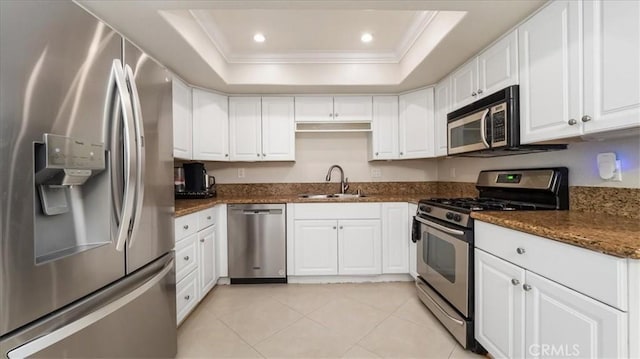 kitchen with appliances with stainless steel finishes, dark stone counters, a raised ceiling, sink, and white cabinetry