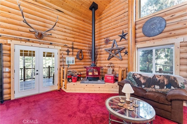 carpeted living room with a towering ceiling, a wood stove, a wealth of natural light, and french doors