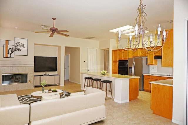 tiled living room with a tiled fireplace and ceiling fan with notable chandelier