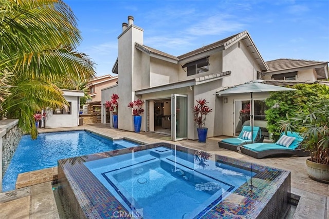 rear view of property featuring a patio, a chimney, stucco siding, an in ground hot tub, and an outdoor pool