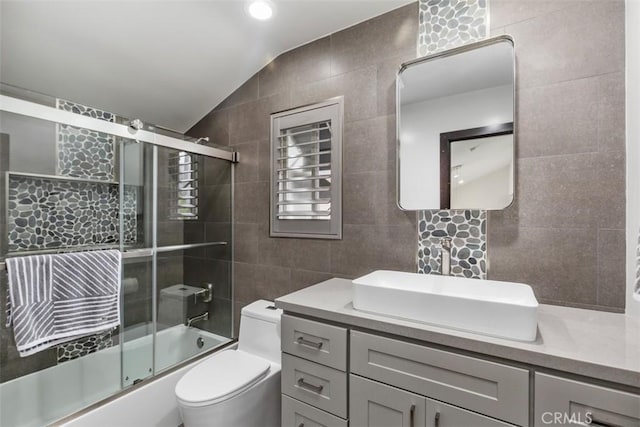 full bath featuring tile walls, lofted ceiling, toilet, combined bath / shower with glass door, and vanity