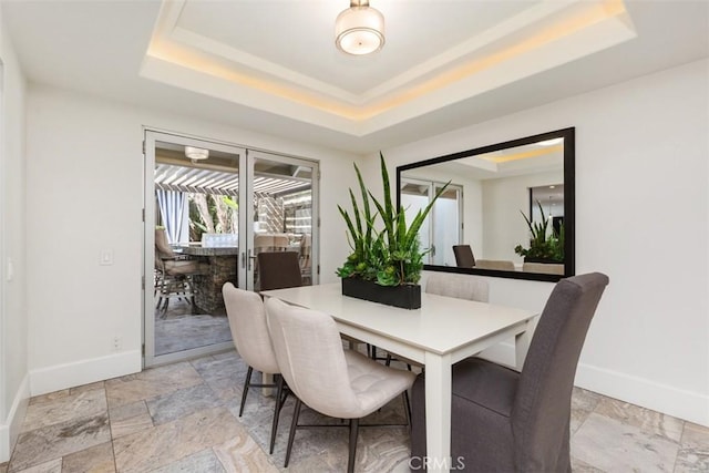 dining space featuring a raised ceiling, stone finish flooring, and baseboards