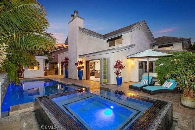 back of property featuring a chimney, a patio area, a pool with connected hot tub, and stucco siding