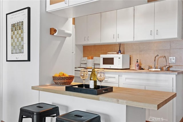 kitchen with white cabinetry, tasteful backsplash, sink, kitchen peninsula, and a breakfast bar