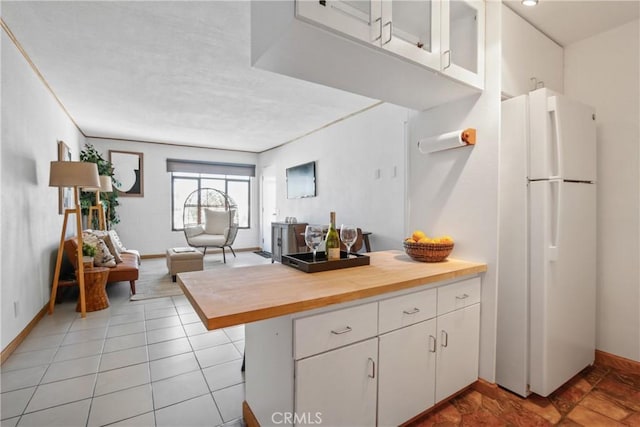 kitchen with white fridge, a kitchen bar, kitchen peninsula, light tile patterned flooring, and white cabinets