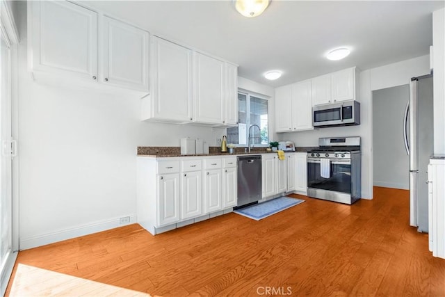 kitchen featuring dark stone counters, sink, light hardwood / wood-style flooring, appliances with stainless steel finishes, and white cabinetry