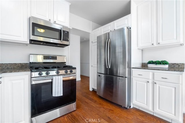 kitchen featuring dark stone countertops, appliances with stainless steel finishes, wood finished floors, and white cabinetry