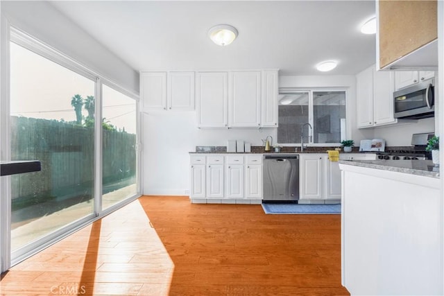 kitchen featuring light stone countertops, appliances with stainless steel finishes, sink, light hardwood / wood-style flooring, and white cabinets