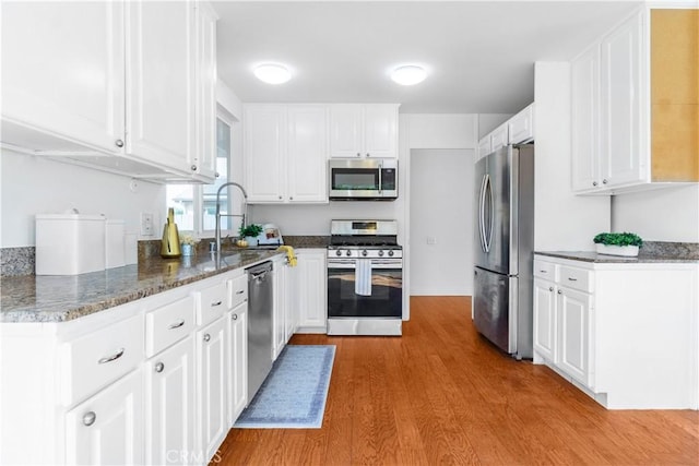 kitchen featuring dark stone counters, white cabinets, sink, light hardwood / wood-style floors, and stainless steel appliances