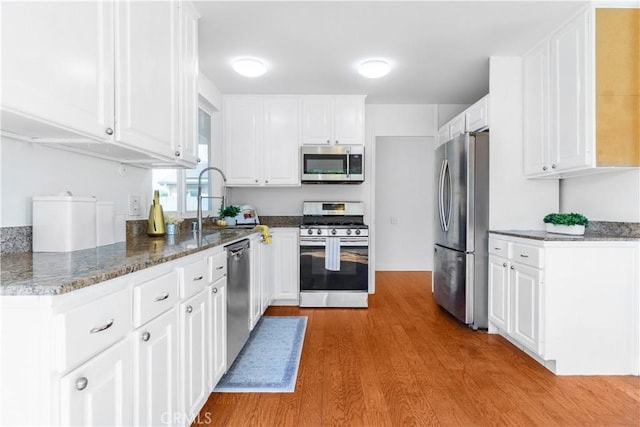 kitchen with a sink, wood finished floors, stainless steel appliances, dark stone counters, and white cabinets