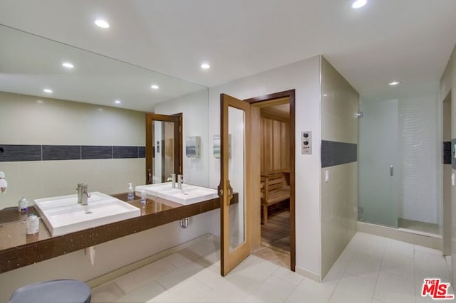 bathroom with tile patterned floors, an enclosed shower, sink, and tile walls