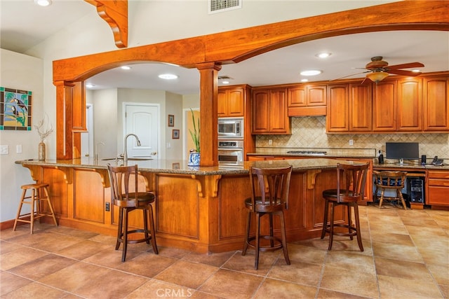 kitchen with a kitchen breakfast bar, ceiling fan, stainless steel appliances, and decorative columns