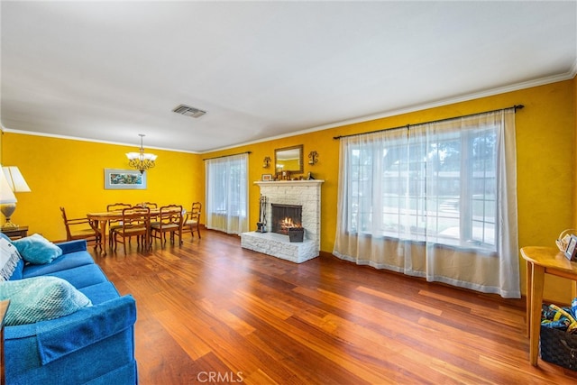 living room featuring ornamental molding, a chandelier, wood-type flooring, and a brick fireplace