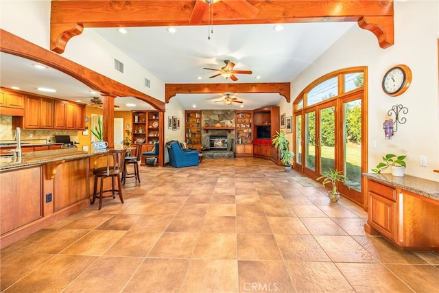 interior space with beam ceiling, a stone fireplace, a kitchen bar, and backsplash