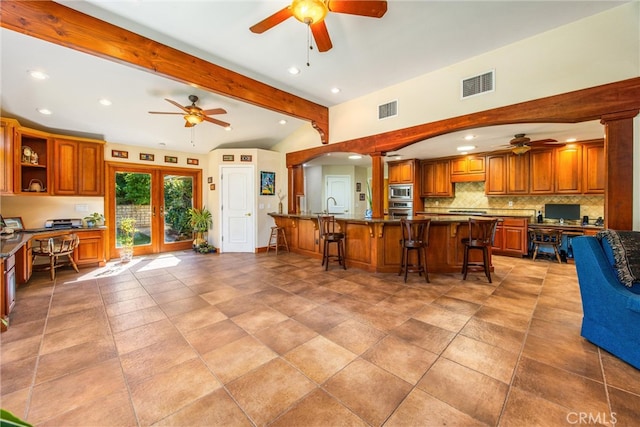 kitchen featuring tasteful backsplash, vaulted ceiling with beams, a kitchen bar, decorative columns, and stainless steel appliances