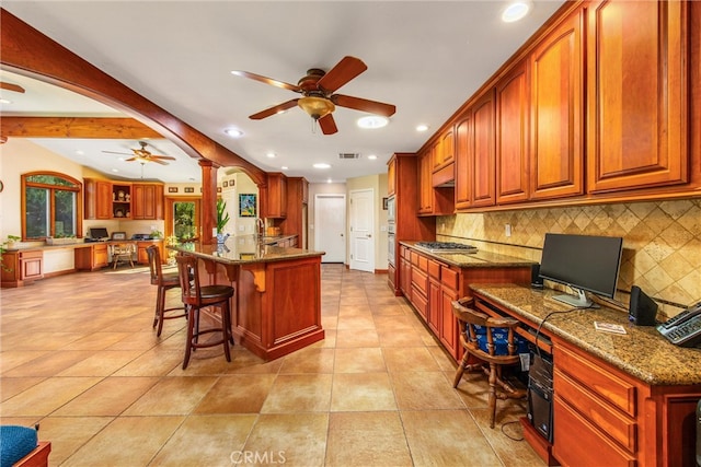 kitchen featuring built in desk, a breakfast bar, backsplash, and dark stone countertops