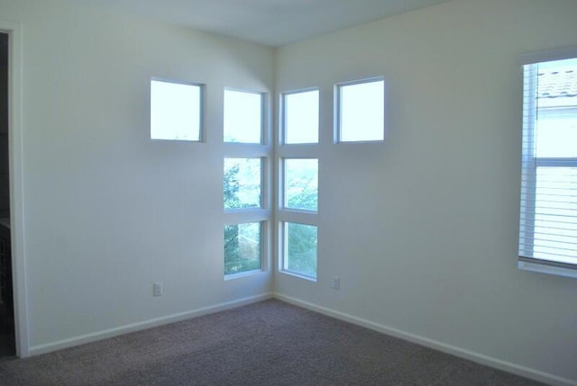 spare room featuring dark carpet and a wealth of natural light