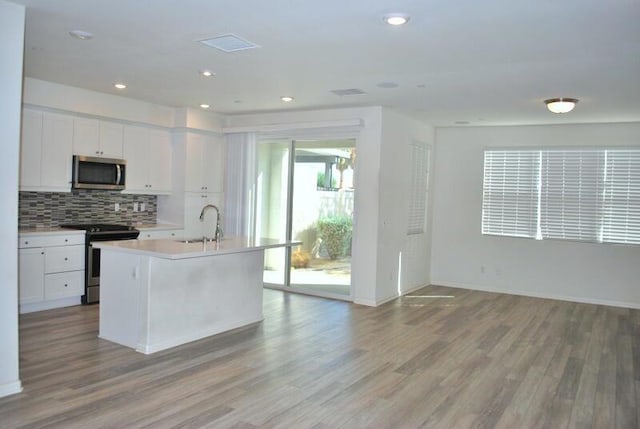 kitchen with appliances with stainless steel finishes, tasteful backsplash, white cabinets, light hardwood / wood-style floors, and an island with sink