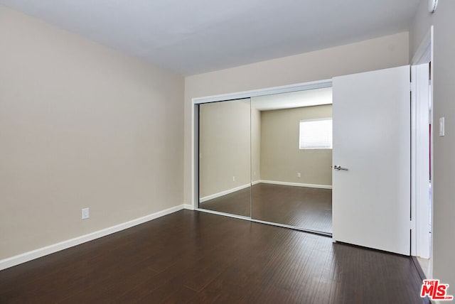 unfurnished bedroom with dark wood-type flooring and a closet