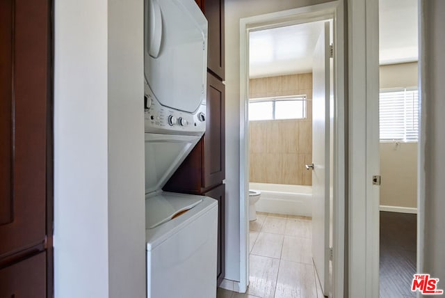 clothes washing area featuring light tile patterned flooring, plenty of natural light, and stacked washer / drying machine