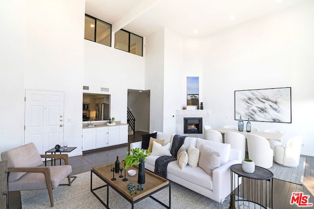 living room featuring beamed ceiling, a high ceiling, hardwood / wood-style flooring, and sink