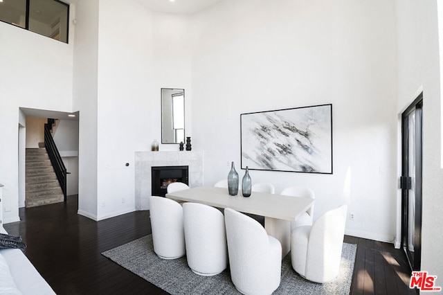 dining space with a high ceiling, dark hardwood / wood-style floors, and a tiled fireplace