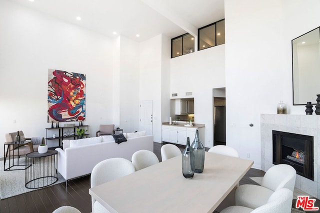 dining area featuring a tile fireplace, a towering ceiling, and dark hardwood / wood-style floors