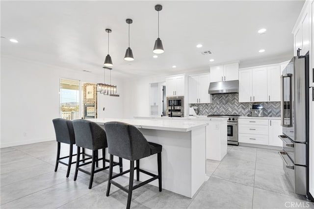 kitchen featuring a center island with sink, decorative light fixtures, high end appliances, light stone countertops, and white cabinets