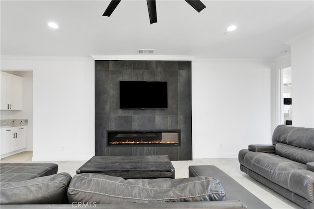 living room with ceiling fan, crown molding, and a tiled fireplace