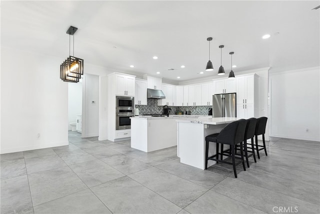 kitchen with a center island with sink, hanging light fixtures, appliances with stainless steel finishes, and white cabinetry