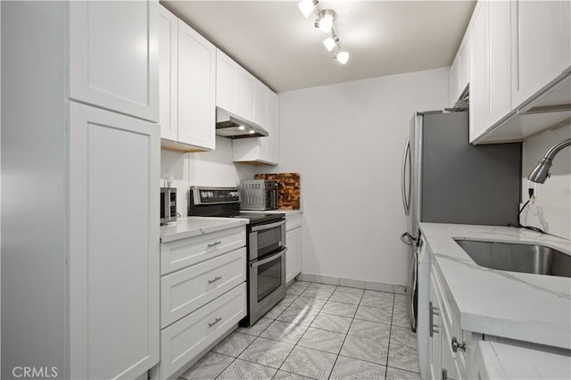 kitchen with sink, white cabinetry, light stone counters, track lighting, and appliances with stainless steel finishes