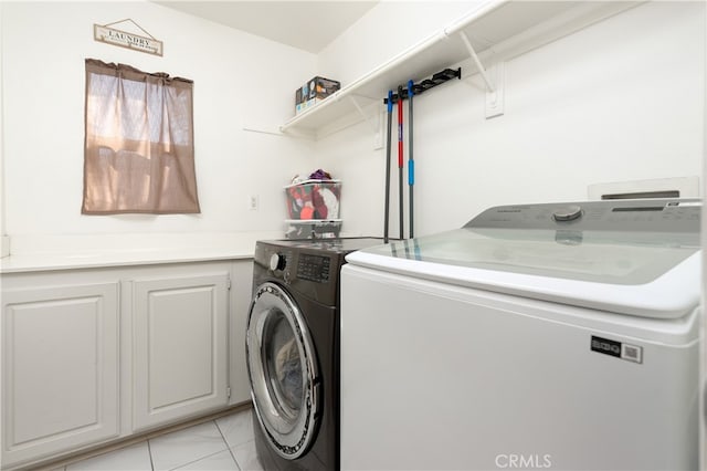 clothes washing area featuring washer and clothes dryer, cabinets, and light tile patterned flooring