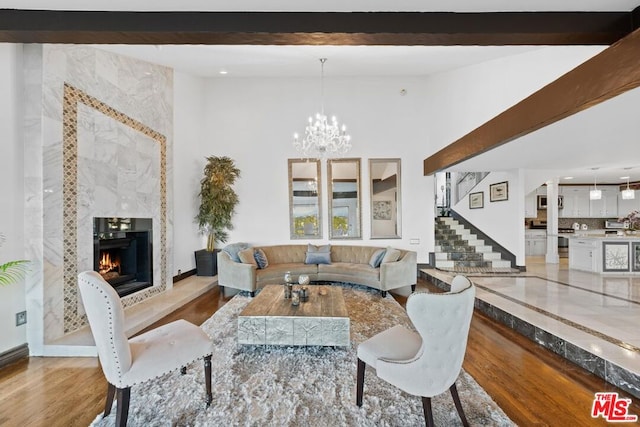 living room featuring beamed ceiling, a chandelier, light hardwood / wood-style floors, and a high end fireplace