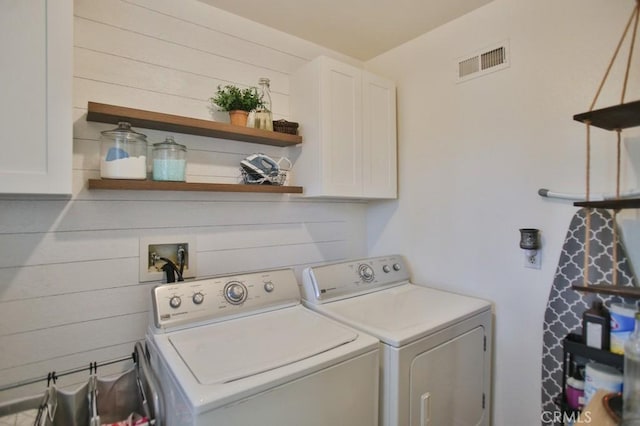 laundry area featuring cabinets, wooden walls, and independent washer and dryer