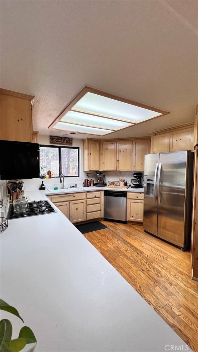 kitchen with appliances with stainless steel finishes, light countertops, light wood-type flooring, light brown cabinets, and a sink