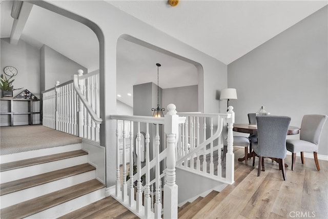 staircase featuring lofted ceiling, wood-type flooring, and an inviting chandelier