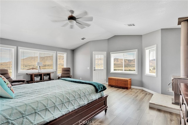 bedroom featuring a wood stove, vaulted ceiling, light hardwood / wood-style flooring, and ceiling fan