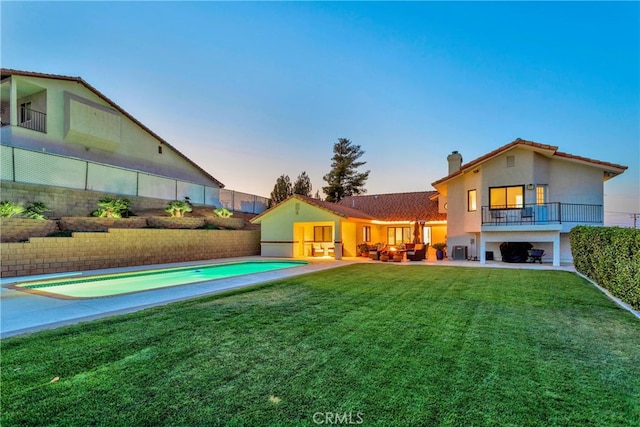 back house at dusk featuring a fenced in pool, a patio, a balcony, and a lawn