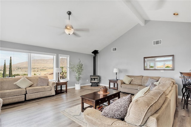 living room with a wood stove, light hardwood / wood-style floors, beam ceiling, and ceiling fan