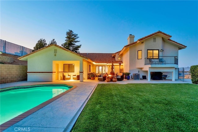 back house at dusk featuring a patio, a balcony, a lawn, and cooling unit