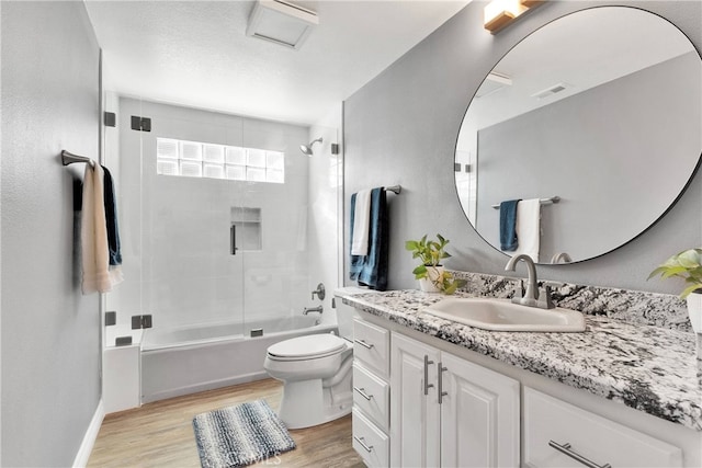 full bathroom featuring hardwood / wood-style floors, combined bath / shower with glass door, toilet, and vanity