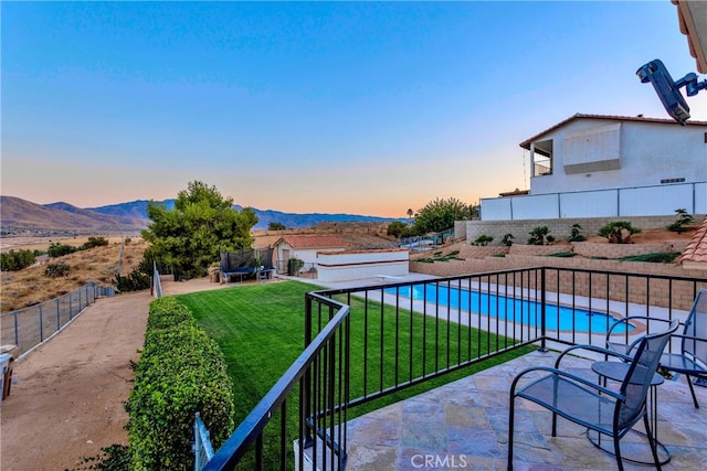 pool at dusk with a mountain view, a lawn, and a patio area